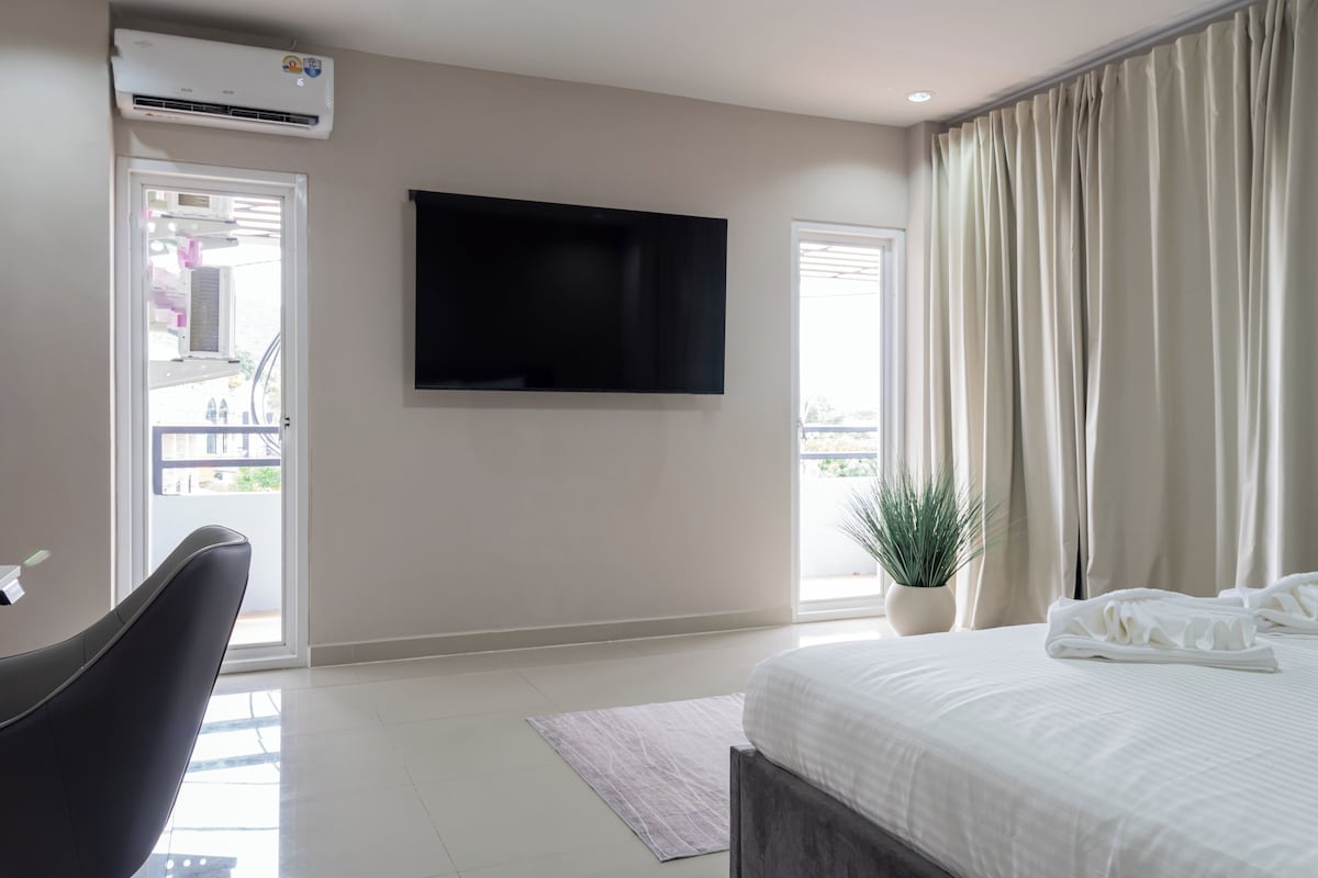 A hotel room with a bed, a flat-screen TV, a potted plant, and a balcony door.