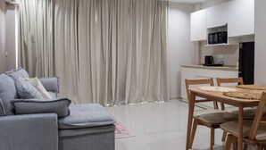 A modern living room with a grey sofa, a dining table with chairs, and a kitchen area with a microwave. - The one Sky (Phuket)