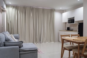 Una sala de estar moderna con un sofá gris, una mesa de comedor con sillas y una zona de cocina con microondas.