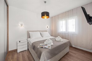 A hotel room with a bed, bedside tables, a reading light, a window with curtains, and a flat-screen TV mounted on the wall. - Vila Mira (Vodice)