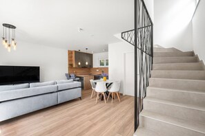 A modern living room with a grey sofa, a flat-screen TV, and a dining area with a white table and chairs. - Vila Mira (Vodice)