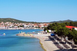 A coastal town with a beach, rows of beach umbrellas, and a clear view of the sea and distant hills. - Vila Mira (Vodice)