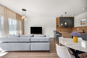 A modern living room with a grey sectional sofa, a flat-screen TV, and a dining area with a marble table. - Vila Mira (Vodice)