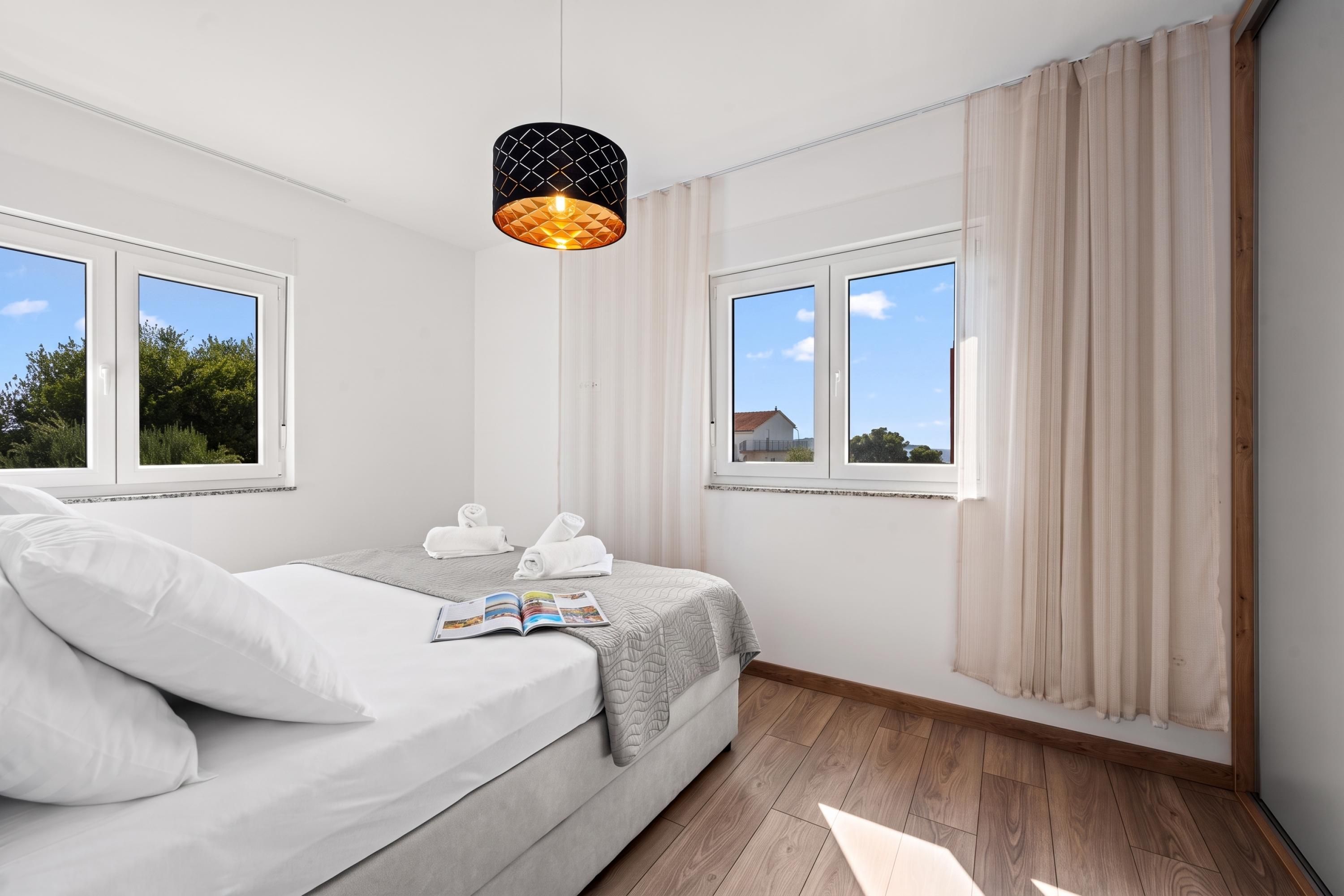 A modern bedroom with a bed, a reading light, and a view of the outside.