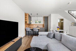 A modern living room with a grey sectional sofa, a flat-screen TV, and a dining area with a white table and chairs. - Vila Mira (Vodice)