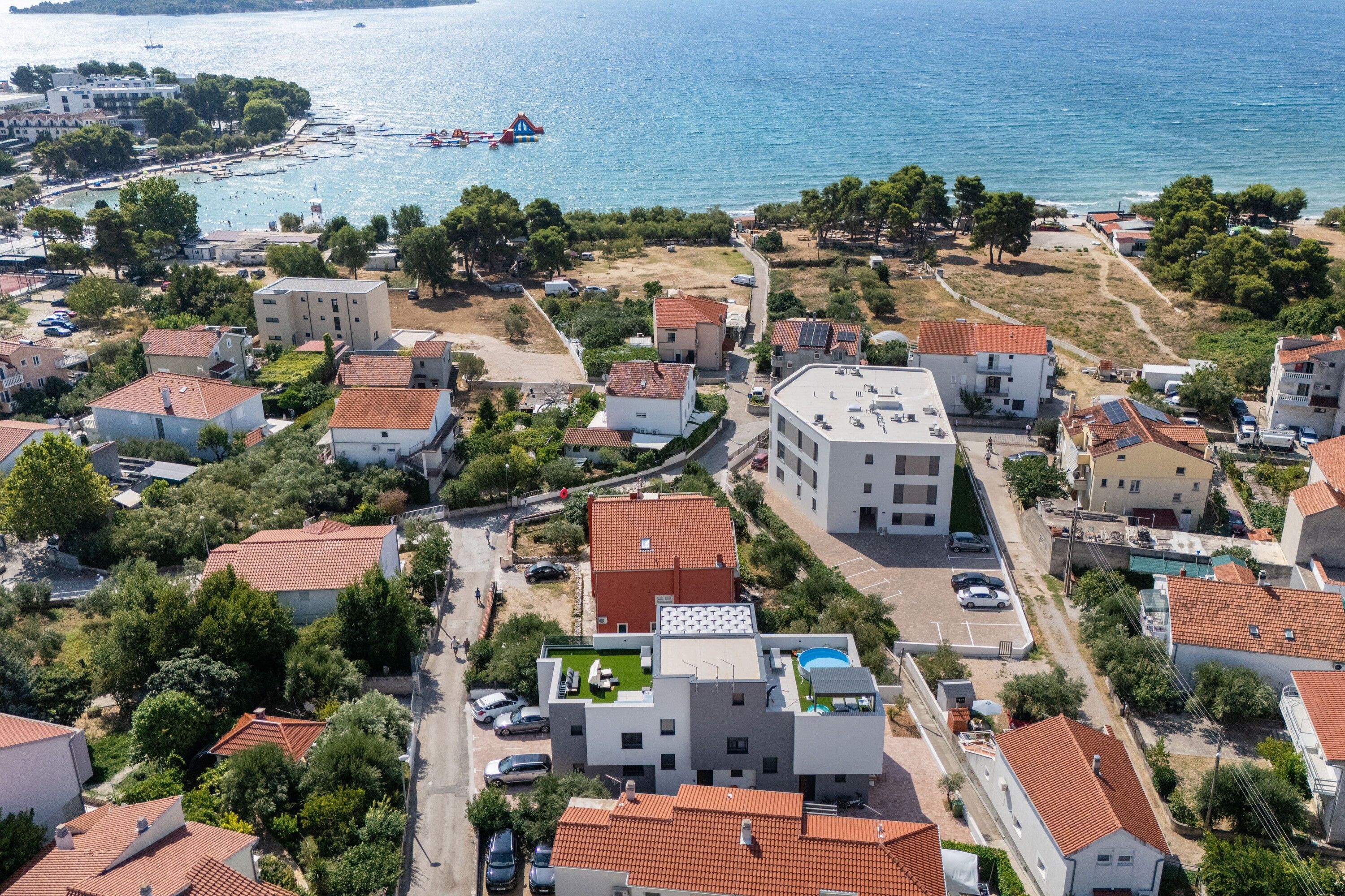Vue aérienne d’une zone résidentielle côtière, avec des maisons, une marina et une vue dégagée sur la mer.