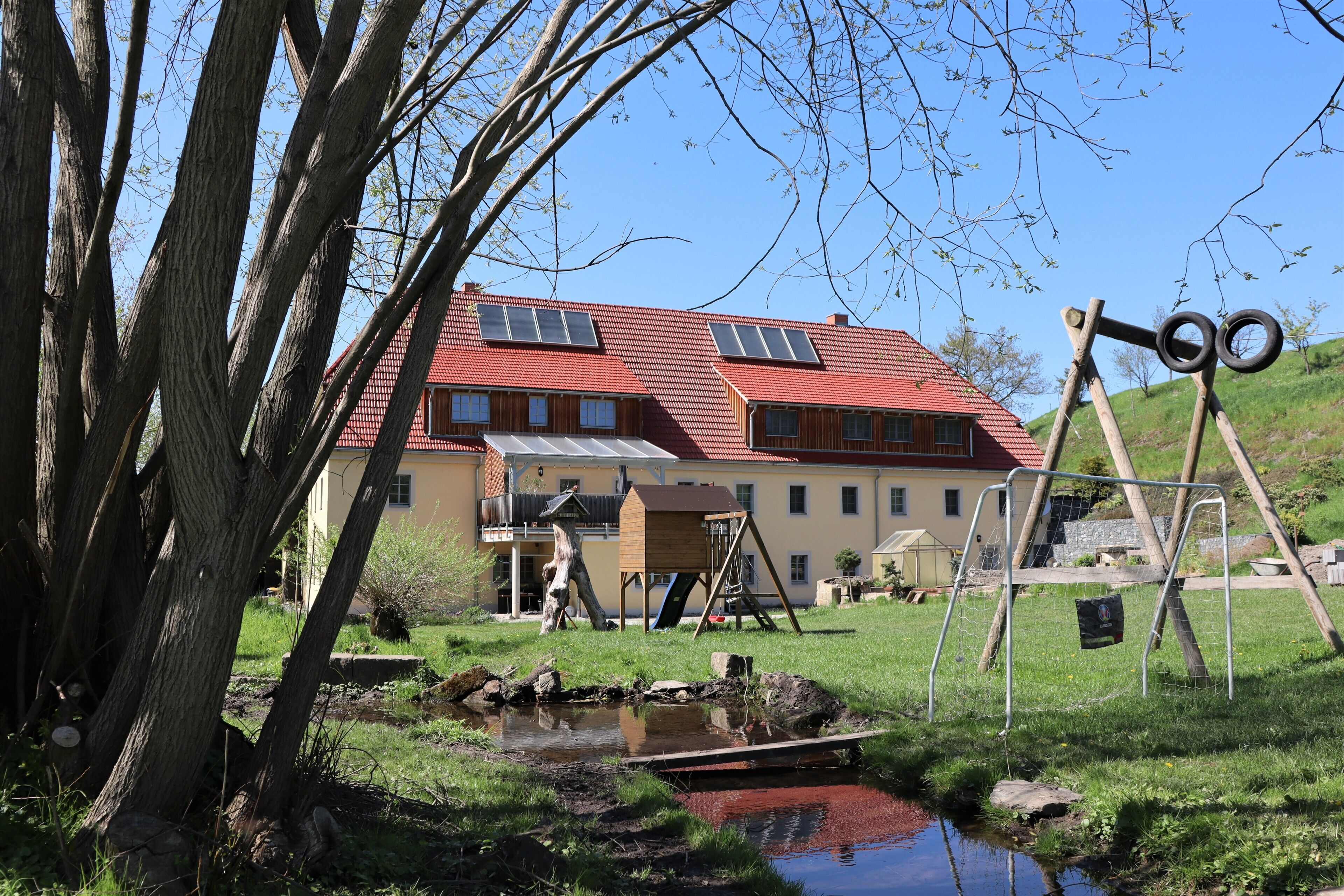 Ein Haus mit rotem Dach, Solaranlagen und einem kleinen Teich.