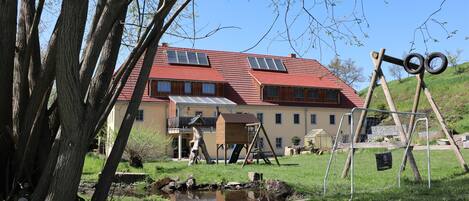 Ein Haus mit rotem Dach, Solaranlagen und einem kleinen Teich.
