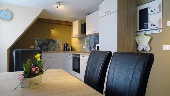 A modern kitchen with white cabinets, a dining table with two chairs, and a clock on the wall. - Vrbo Property (Bahretal)