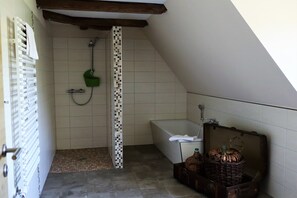 A small, sloped-roofed bathroom with a shower, a bathtub, and a tiled floor. - Vrbo Property (Bahretal)