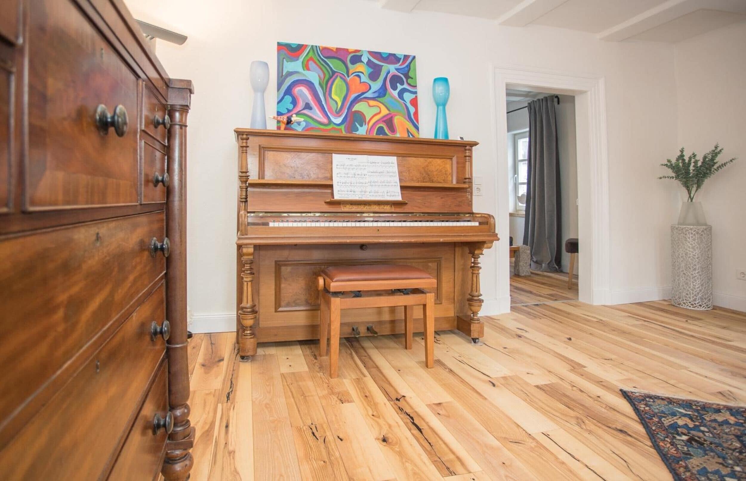 Ein Holzpiano mit Noten, eine Bank und ein farbenfrohes abstraktes Gemälde darüber.