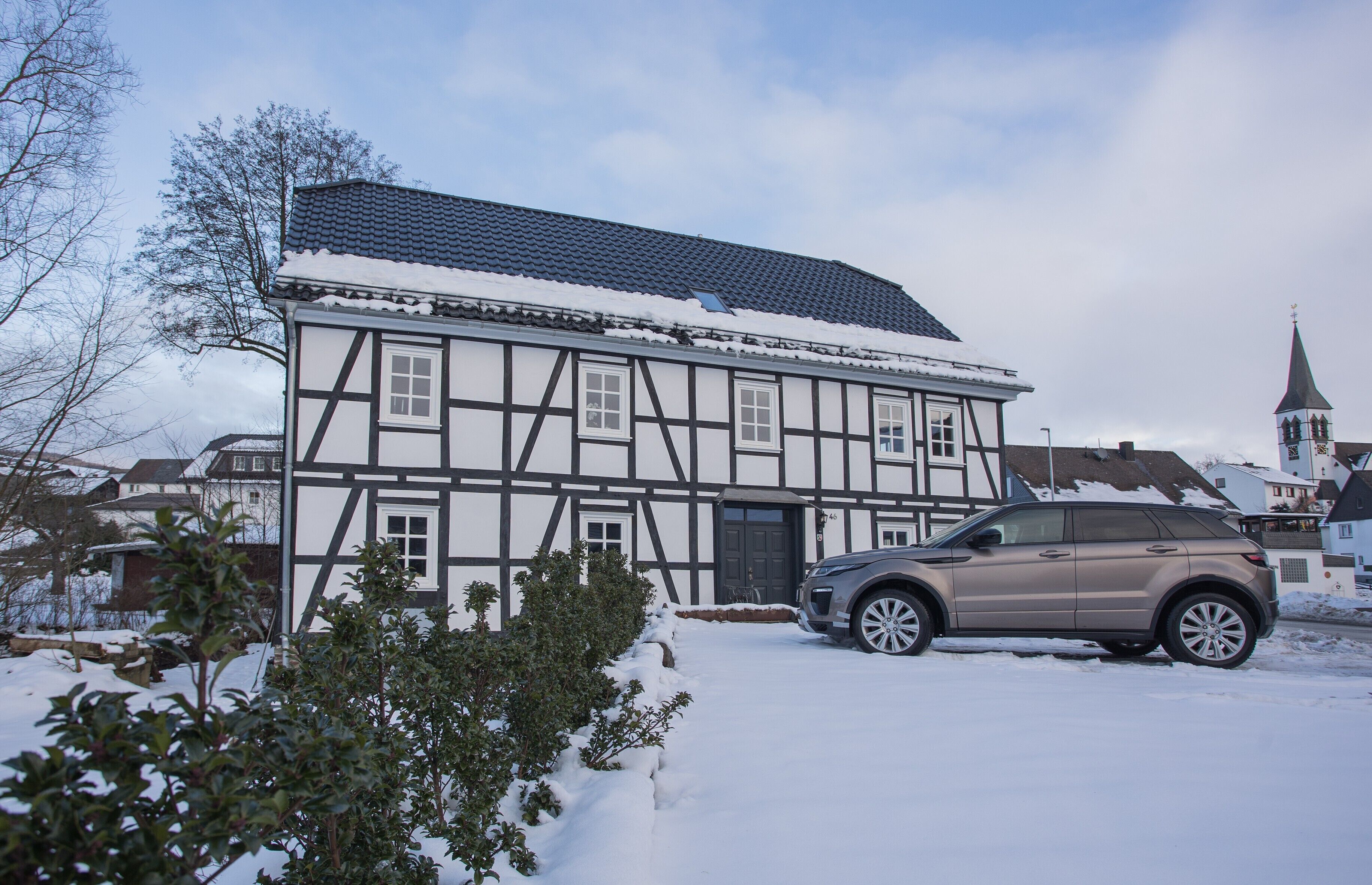 A traditional half-timbered house with a car parked in front, surrounded by snow.