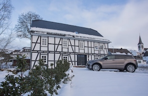 A traditional half-timbered house with a car parked in front, surrounded by snow.