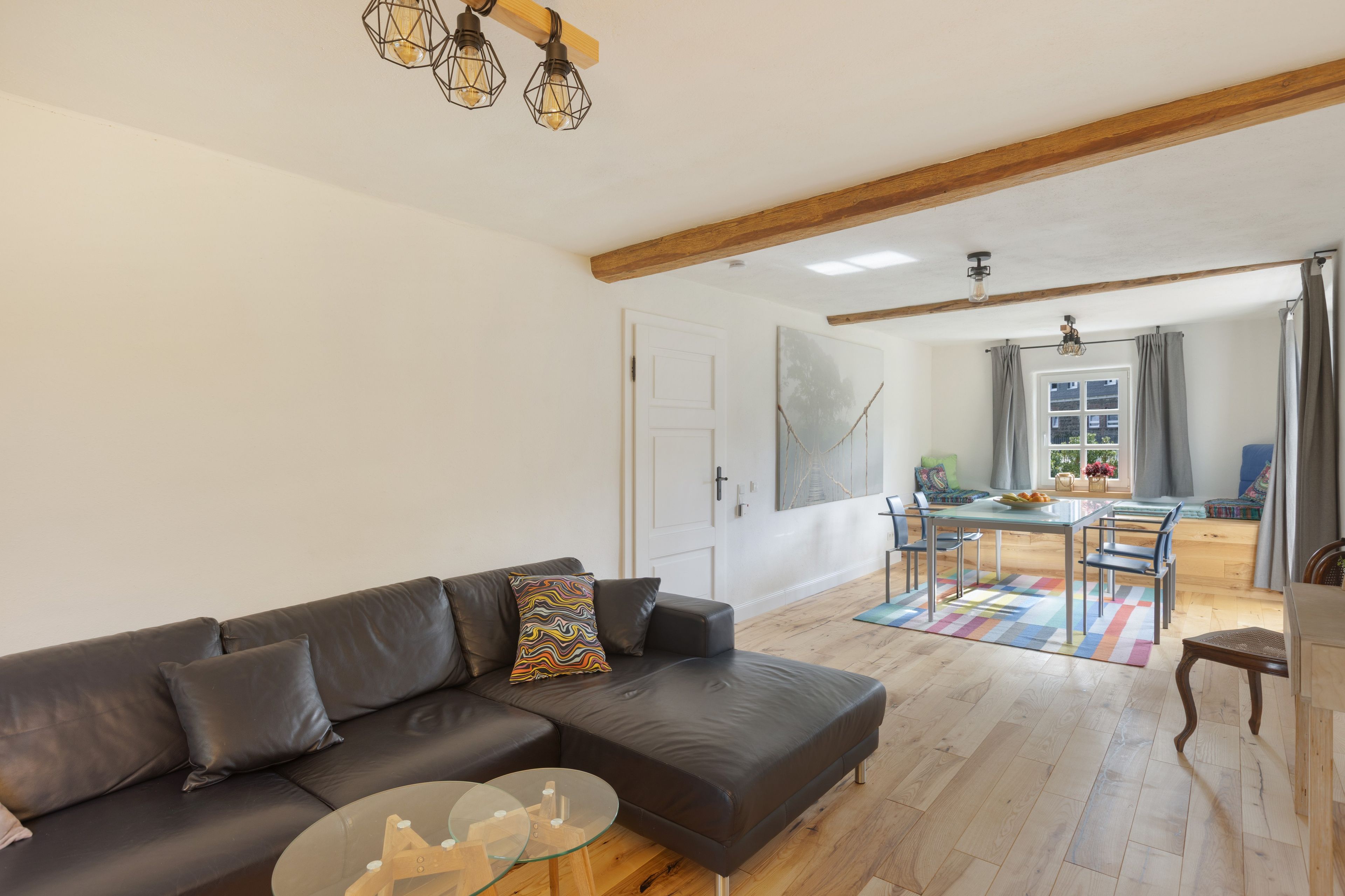Una sala de estar moderna con un sofá de cuero, una mesa de centro de vidrio y un comedor con mesa y sillas de madera.