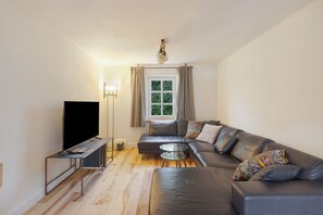A modern living room with a leather sofa, a glass coffee table, a flat-screen TV, and a window with curtains.