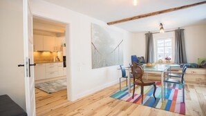 A modern kitchen with white cabinets, a dining area with a glass table and chairs, and a colorful rug. - Apartment 'Denkmal Haus Hugo EG' with Private Terrace, Shared Garden and Wi-Fi (Medebach)