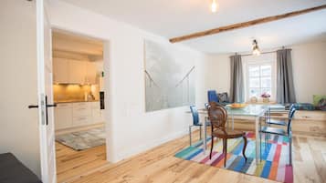 Een moderne keuken met witte kasten, een eethoek met een glazen tafel en stoelen, en een kleurrijk vloerkleed.