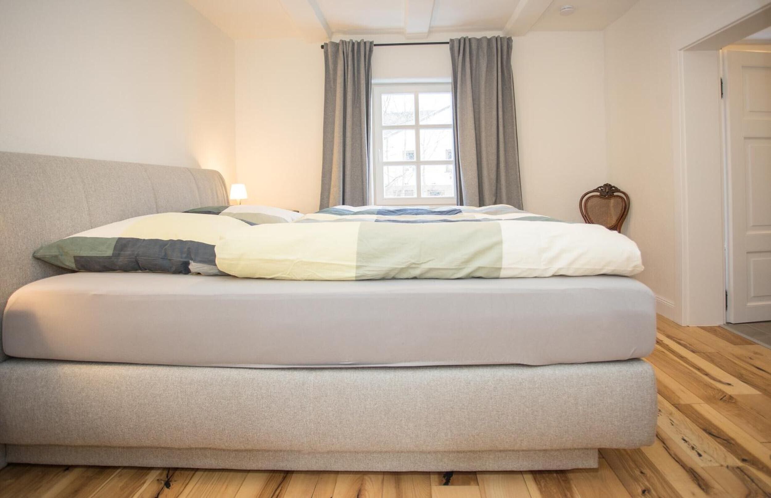 Een moderne slaapkamer met een groot bed, een raam met gordijnen en een houten vloer.