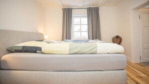 A modern bedroom with a large bed, a window with curtains, and a wooden floor. - Apartment 'Denkmal Haus Hugo EG' with Private Terrace, Shared Garden and Wi-Fi (Medebach)