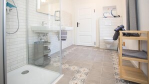 A bathroom with a glass shower enclosure, a sink, a toilet, and a wooden shelf with towels. - Apartment 'Denkmal Haus Hugo EG' with Private Terrace, Shared Garden and Wi-Fi (Medebach)