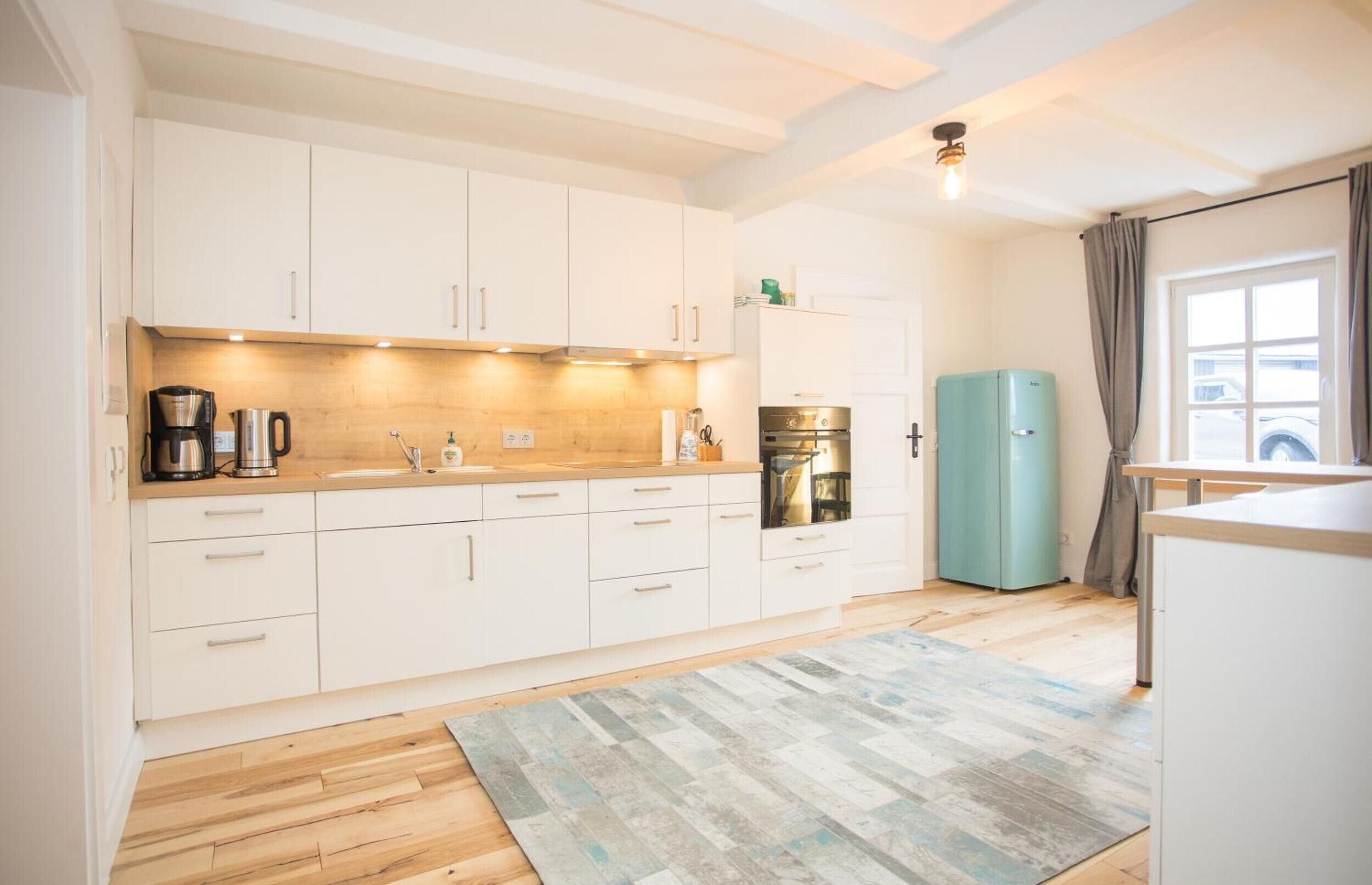 A modern kitchen with white cabinets, a coffee maker, a kettle, and a refrigerator.