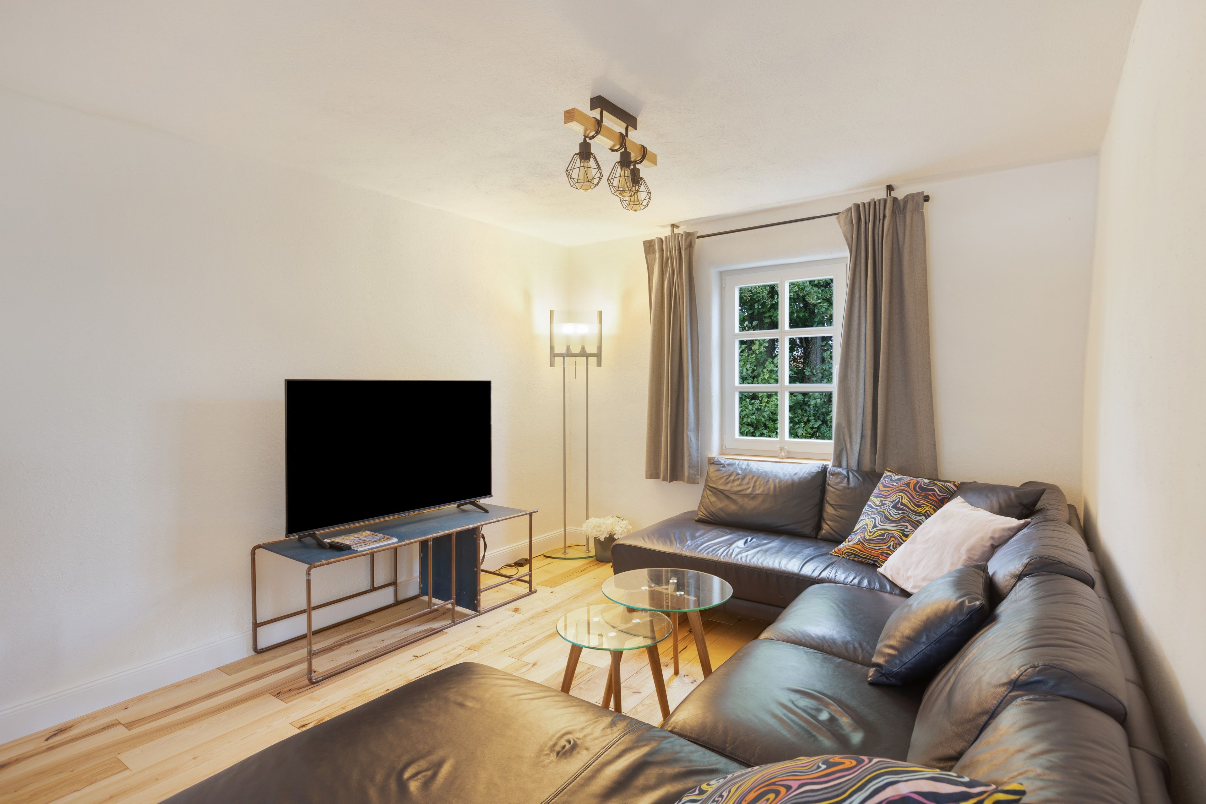 A modern living room with a leather sofa, a glass coffee table, a flat-screen TV, and a floor lamp.