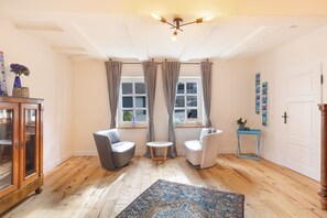 A room with a wooden floor, a blue rug, a cabinet, two chairs, a small table, and a door. - Apartment 'Denkmal Haus Hugo EG' with Private Terrace, Shared Garden and Wi-Fi (Medebach)