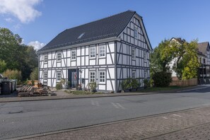 A traditional half-timbered building with a tiled roof, located on a street with a paved road and a sidewalk.
