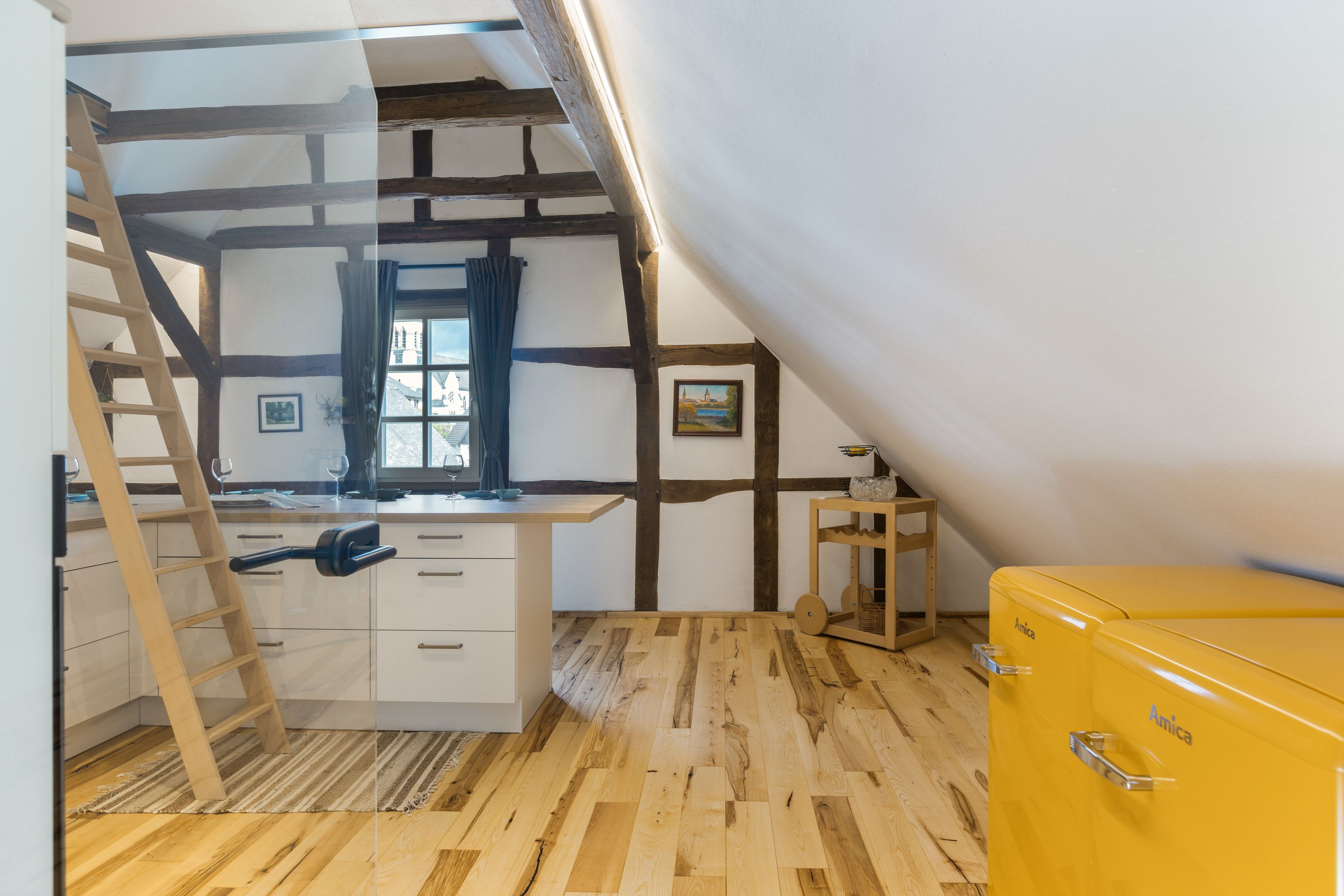 Ein Zimmer mit Schlafkoje, Schreibtisch, einem Fenster mit Vorhängen und einem gelben Schrank.