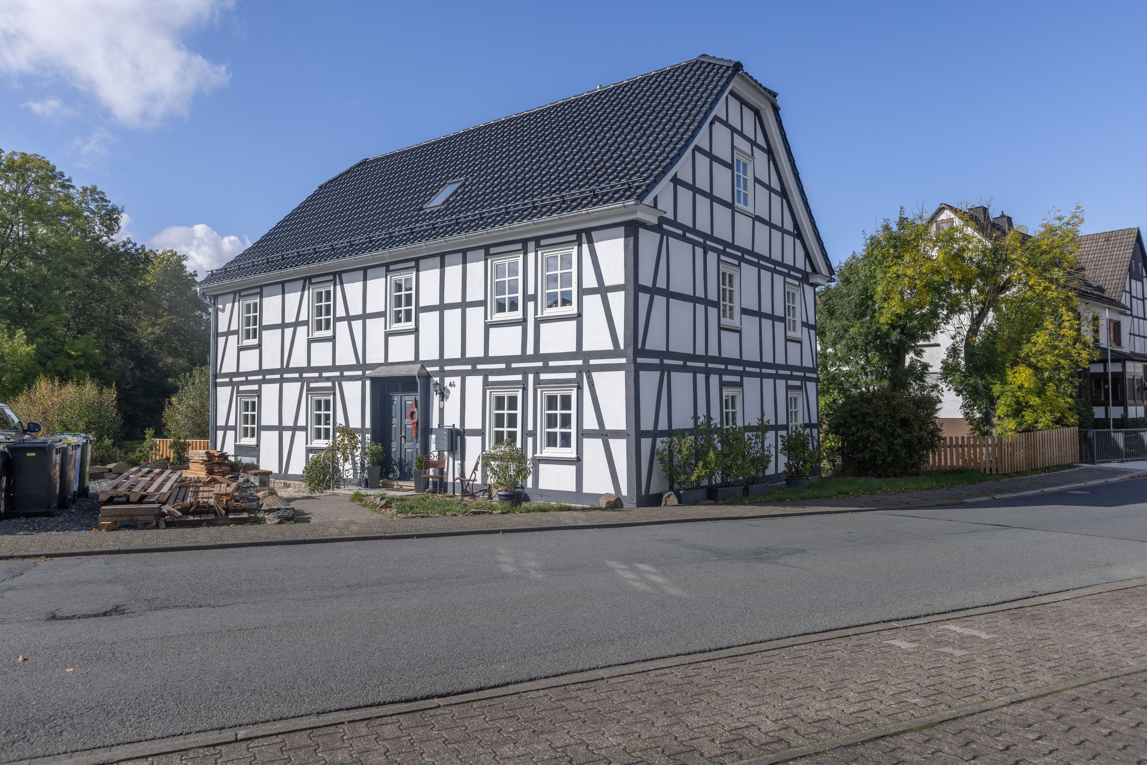 A traditional half-timbered building with a tiled roof, located on a street with a paved road and a sidewalk.