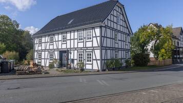A traditional half-timbered building with a tiled roof, located on a street with a paved road and a sidewalk.