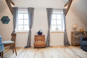 A room with wooden flooring, a wooden dresser, a chair, a table with a lamp, and a window with curtains. - Denkmal Haus Hugo Loft Apartment with Alpine Flair and Wi-Fi (Medebach)