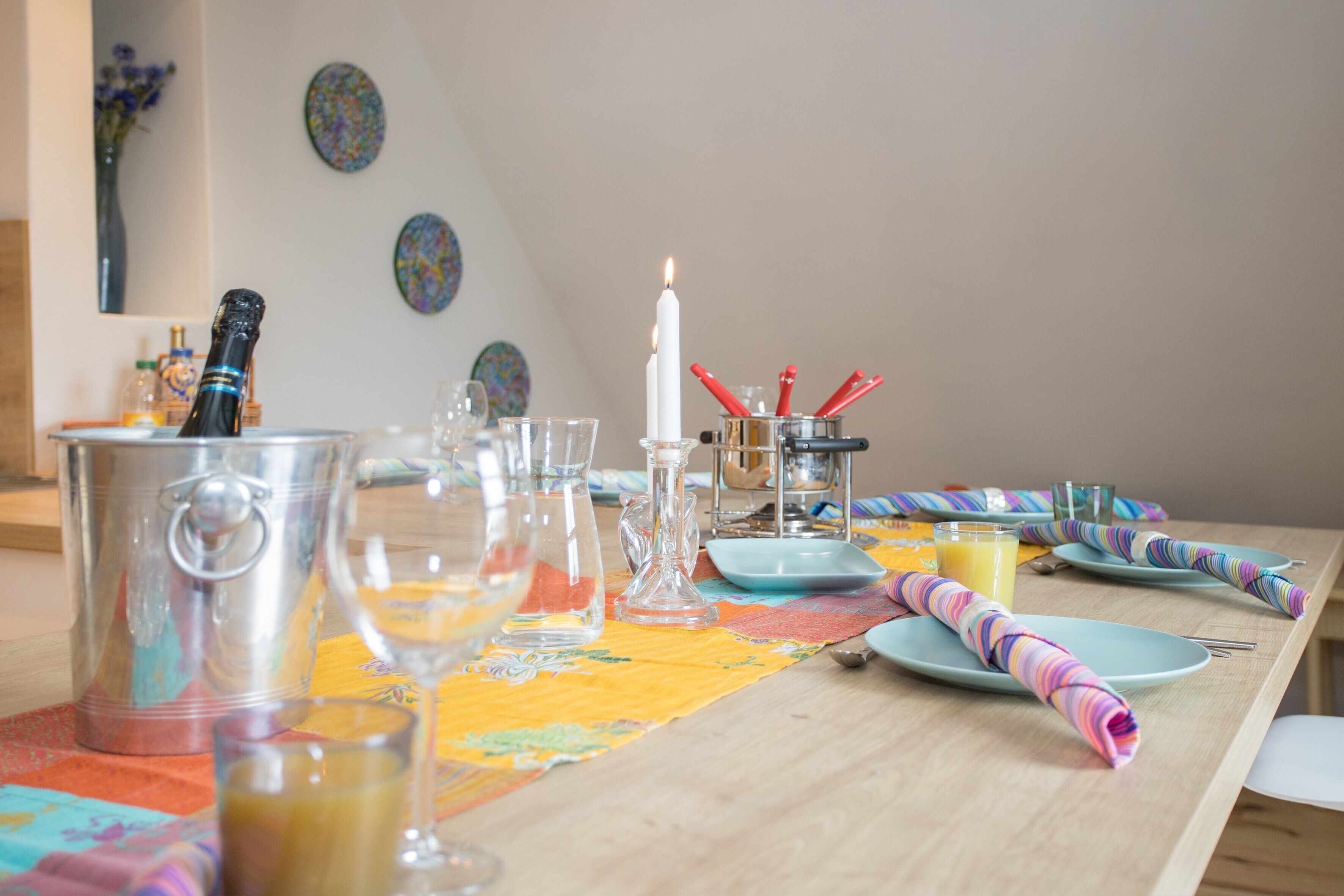 Een eettafel gedekt met verschillende glazen, een kaars en een kleurrijke tafelkleed.