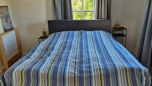 Een slaapkamer met een bed, een raam en een nachtkastje.