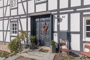 A half-timbered building with a dark entrance door, a number plaque, and a small porch area with a wicker chair and potted plants. - Apartment Denkmal Haus Hugo OG and Wi-Fi (Medebach)