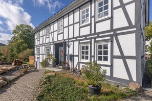 Un bâtiment traditionnel à colombages, doté d’une entrée pavée et d’un jardin agrémenté de plantes en pot.