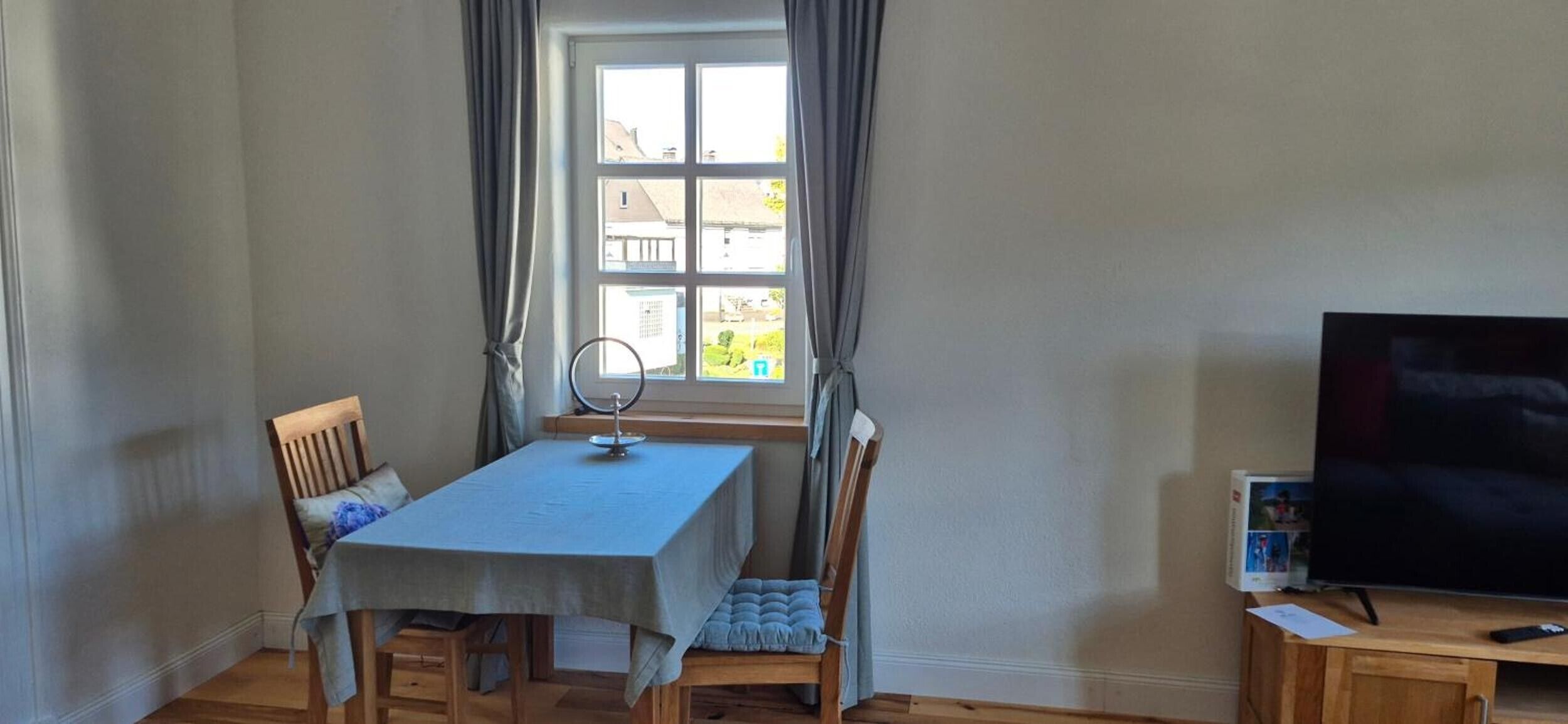 Een kamer met een tafel, stoelen, een televisie en een raam met gordijnen.