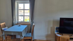 Een kamer met een tafel, stoelen, een televisie en een raam met gordijnen.