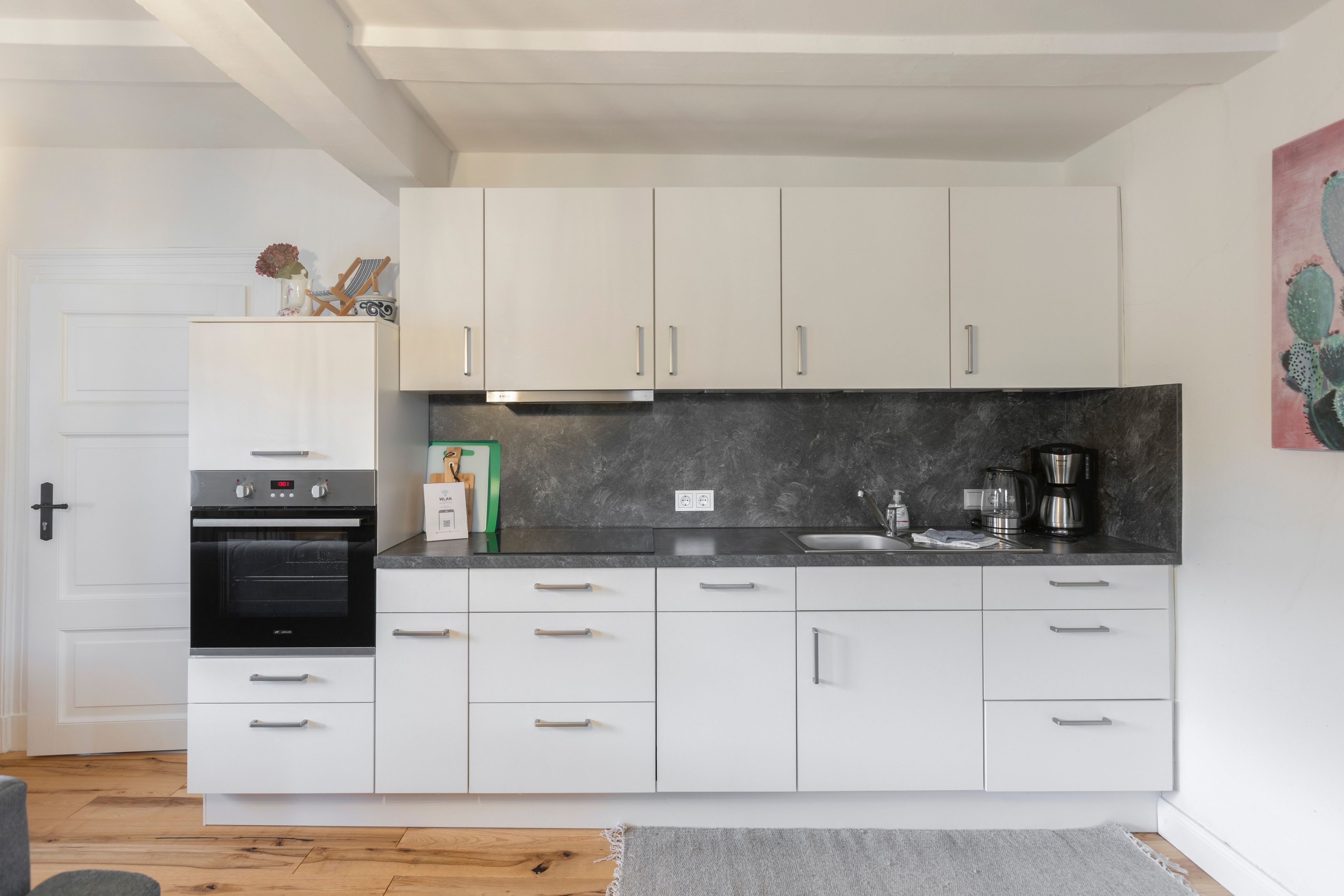A modern kitchen with white cabinets, a built-in oven, and a coffee maker.