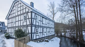 Een vakwerkhuis met een rivier ervoor, houten omheining en sneeuw op de grond.