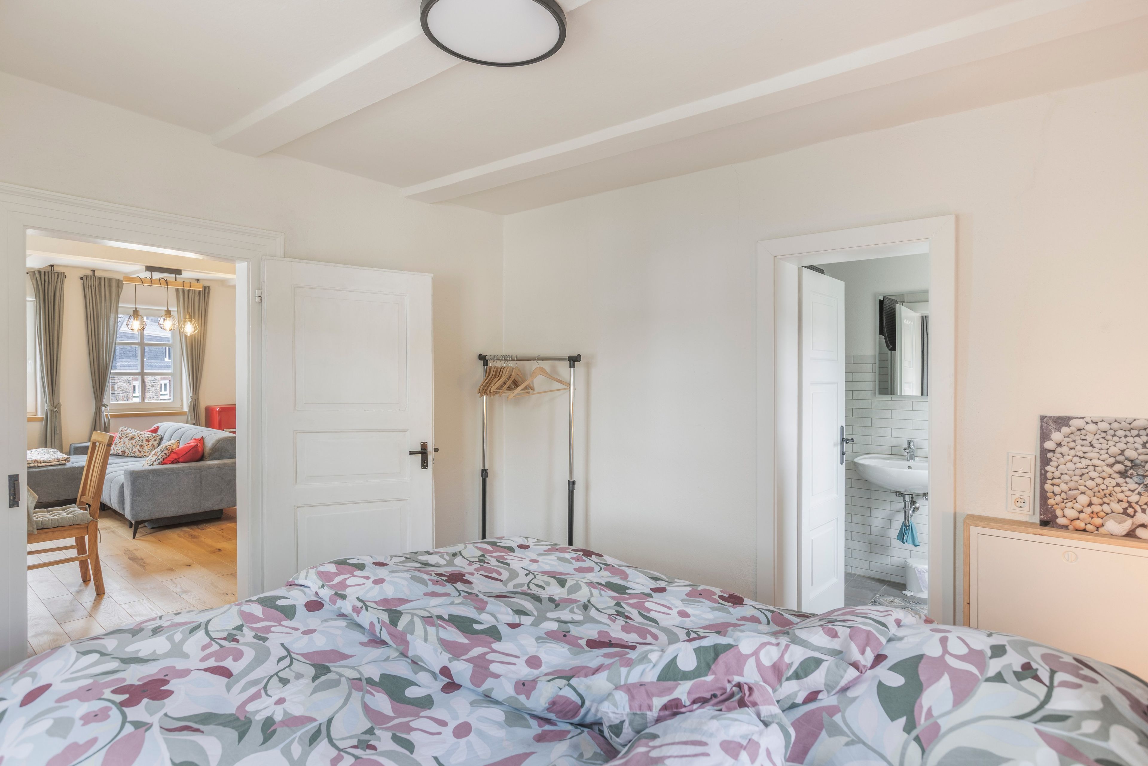 Een slaapkamer met een bed, een kledingkast, een deur naar een badkamer en uitzicht op een woonkamer.