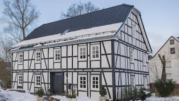 Uma casa tradicional em estilo meio-madeira, com telhado íngreme, várias janelas e o número 46 visível na fachada.
