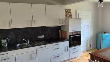 Eine kompakte Küche mit weißen Schränken, einer schwarzen Arbeitsplatte, einem Spülbecken und einem kleinen, blauen Kühlschrank.