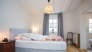 A bedroom with a bed, a nightstand, a chair, a window with curtains, and a hanging light fixture. - Denkmal Haus Hugo OG Apartment with Garden View and Wi-Fi (Medebach)
