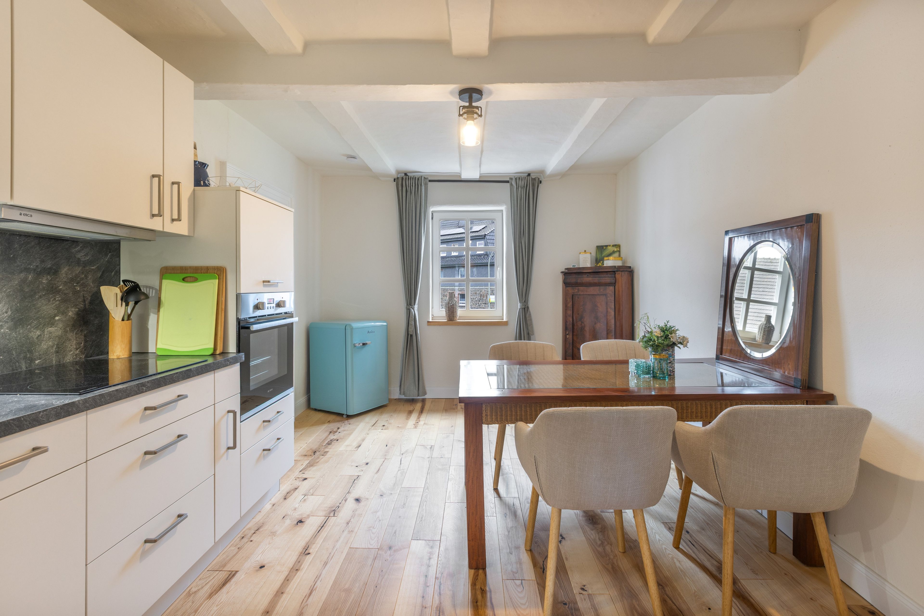Cozinha compacta com eletrodomésticos modernos, área de jantar com mesa e cadeiras de madeira, e vista pela janela.