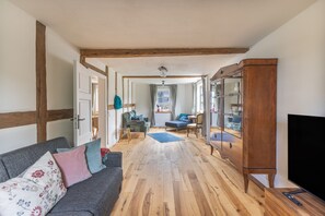 A spacious living room with a wooden floor, a sofa with patterned cushions, a television, and a large wooden cabinet. - Denkmal Haus Hugo OG Apartment with Garden View and Wi-Fi (Medebach)