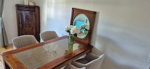 Une table à manger avec un vase de fleurs, des chaises, un miroir et un buffet.
