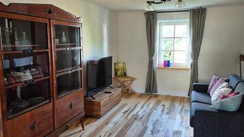 Ein Wohnzimmer mit Holzschrank, Fernseher, kleinem Tisch und einer Couch.