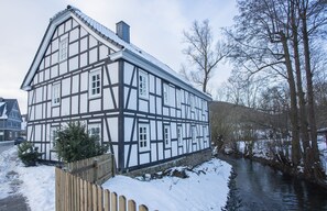 Une maison à colombages, avec une rivière en contrebas, une clôture en bois et de la neige au sol.