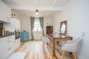 Eine kompakte Küche mit modernen Geräten, ein Essbereich mit einem Holztisch und Stühlen sowie ein Fenster mit Vorhängen.